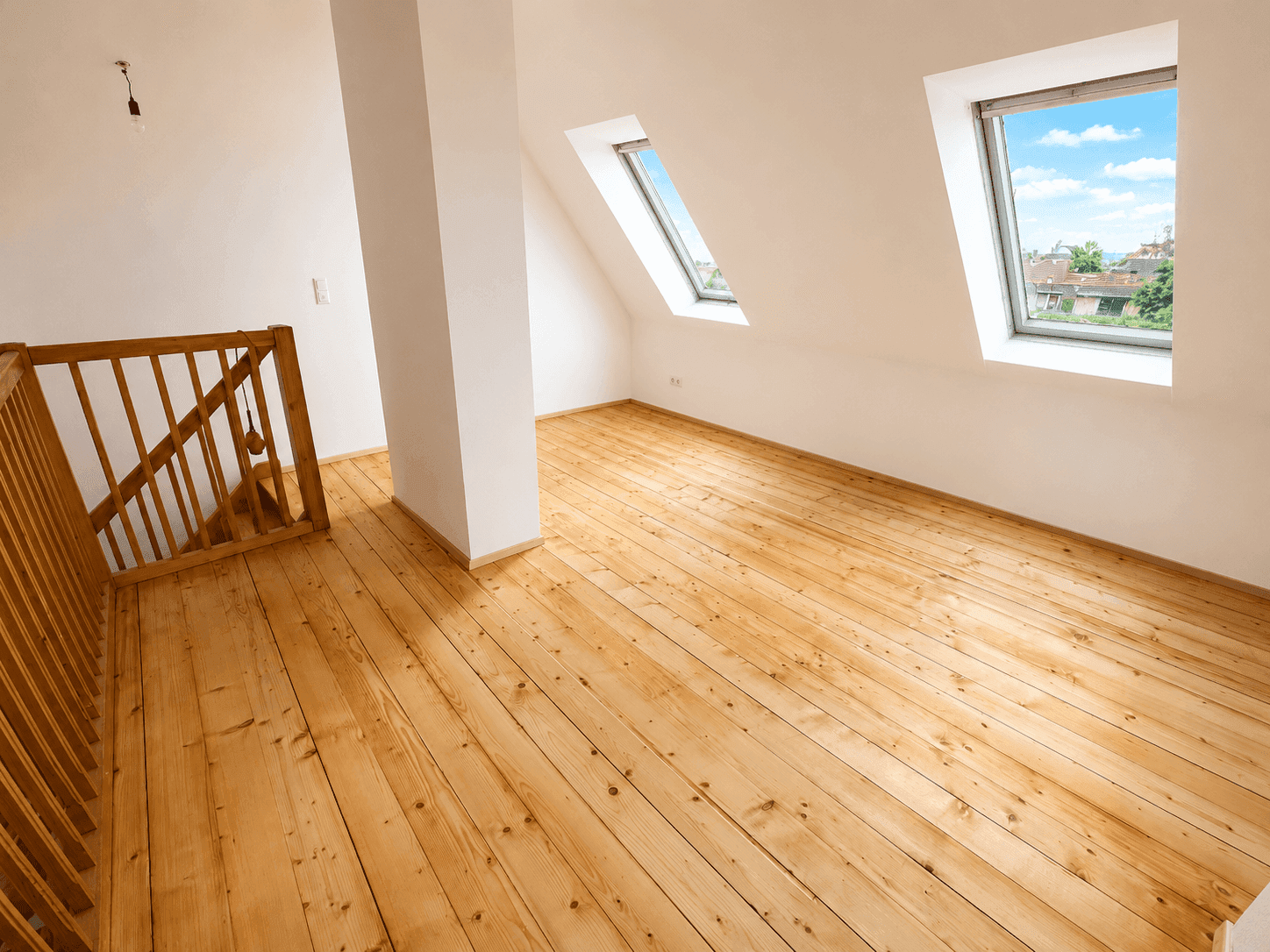 Geräumiges Wohnzimmer im Dachgeschoss mit Holzdielenboden und Dachfenstern.