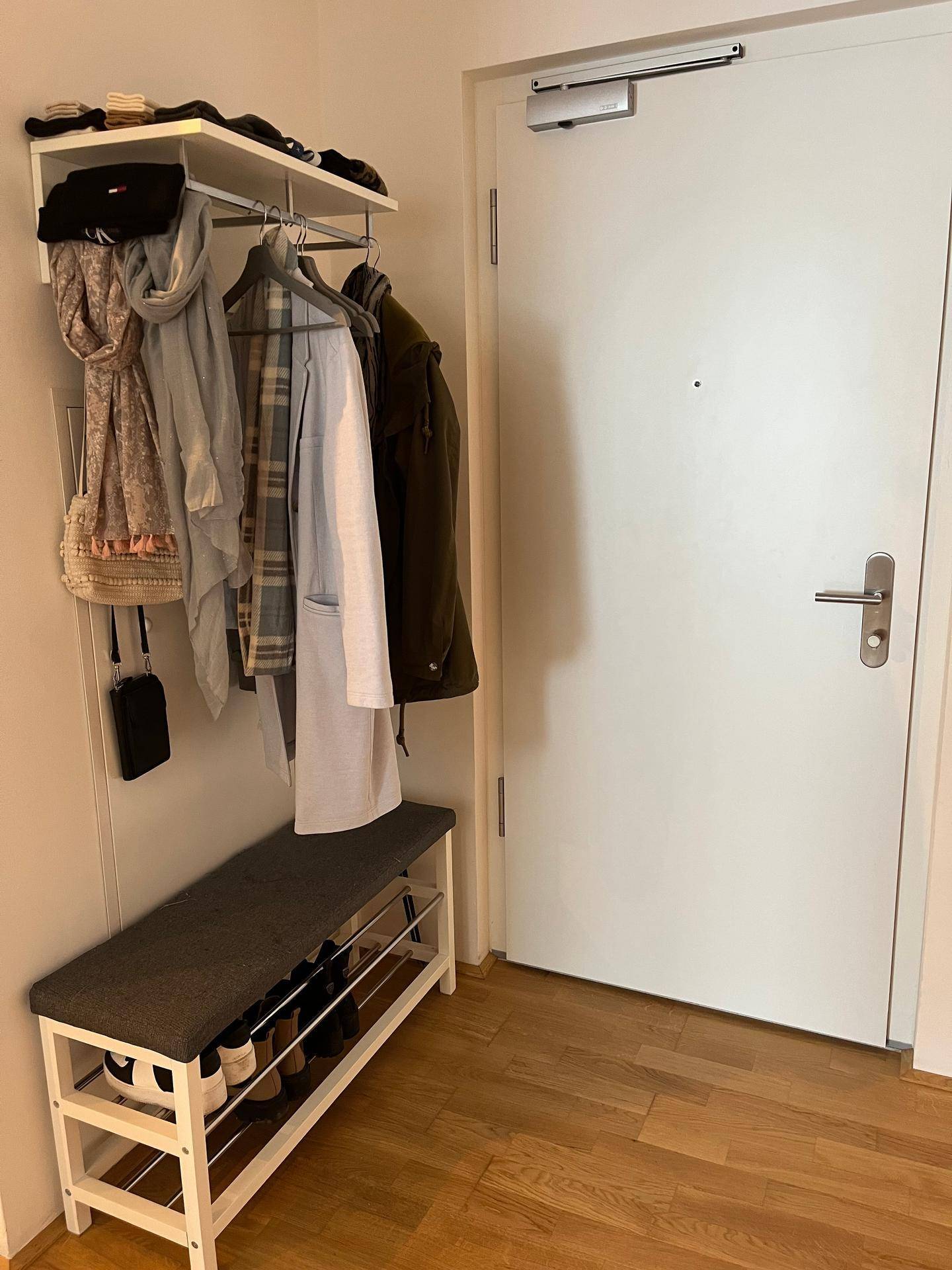 Eingangsbereich mit Garderobe, Schuhregal und heller Holztür.