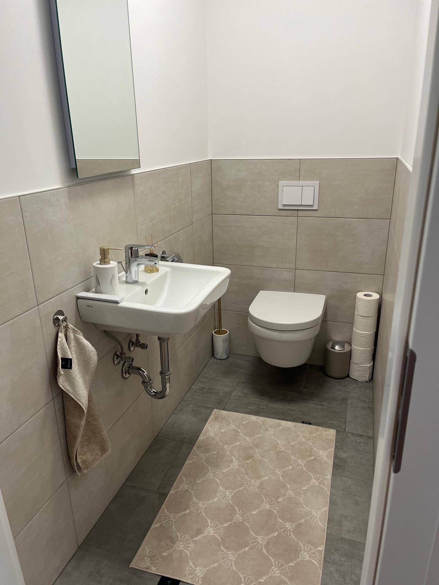 Helles Gäste-WC mit wandhängender Toilette, Waschbecken und Fliesenboden.