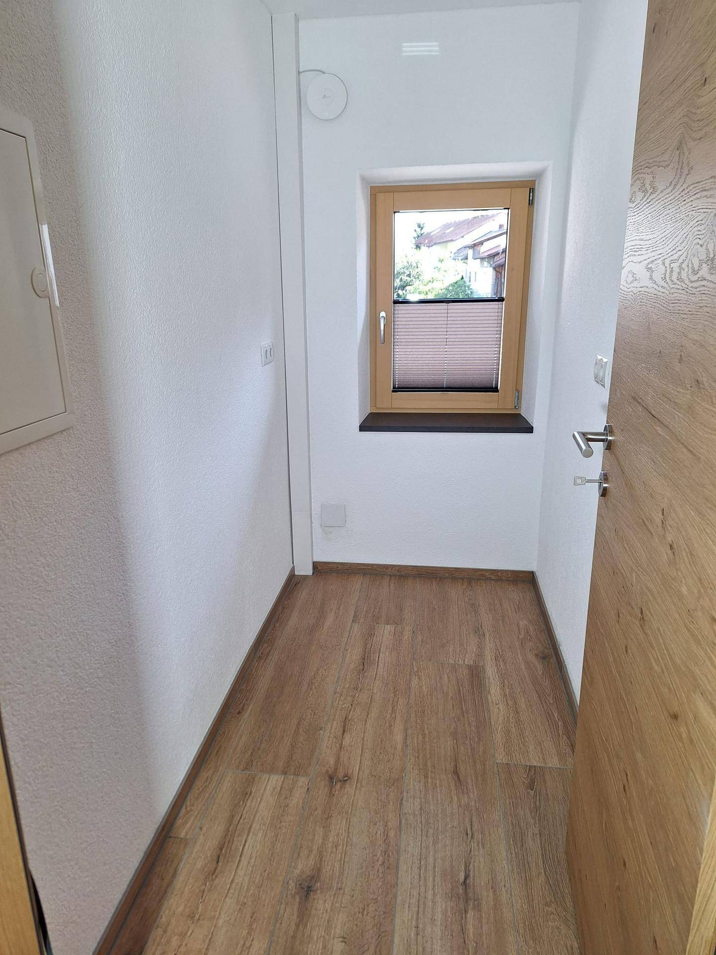 Heller Flur mit Holzboden und einem Fenster, das Tageslicht hereinlässt.