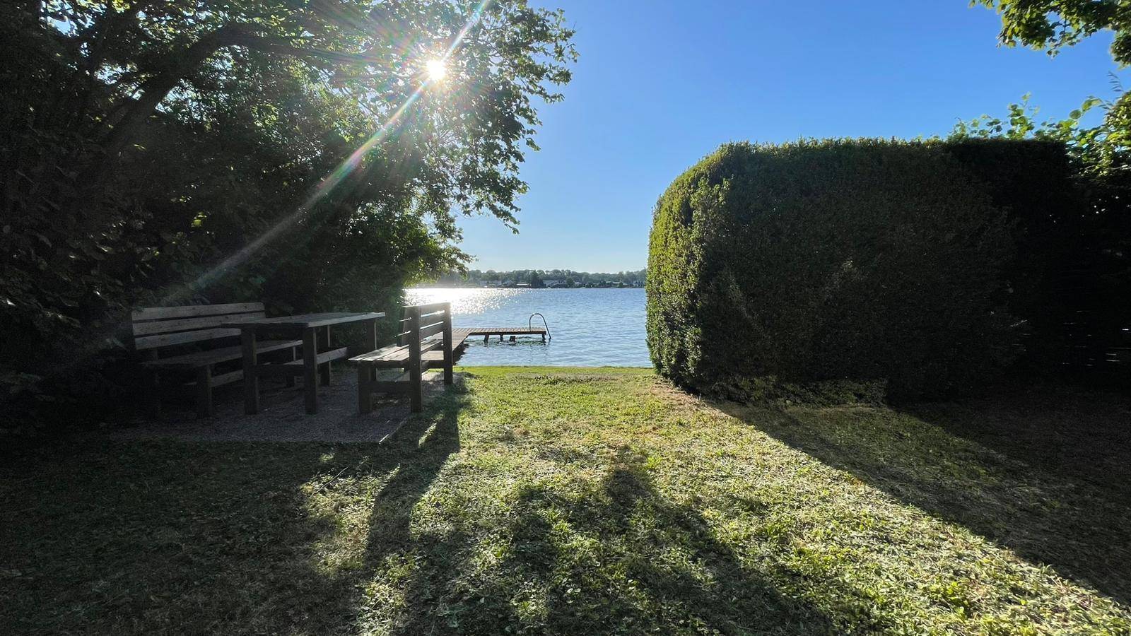 Gepflegter Gartenbereich mit rustikaler Sitzgruppe und direktem Blick auf den See und den Holzsteg.