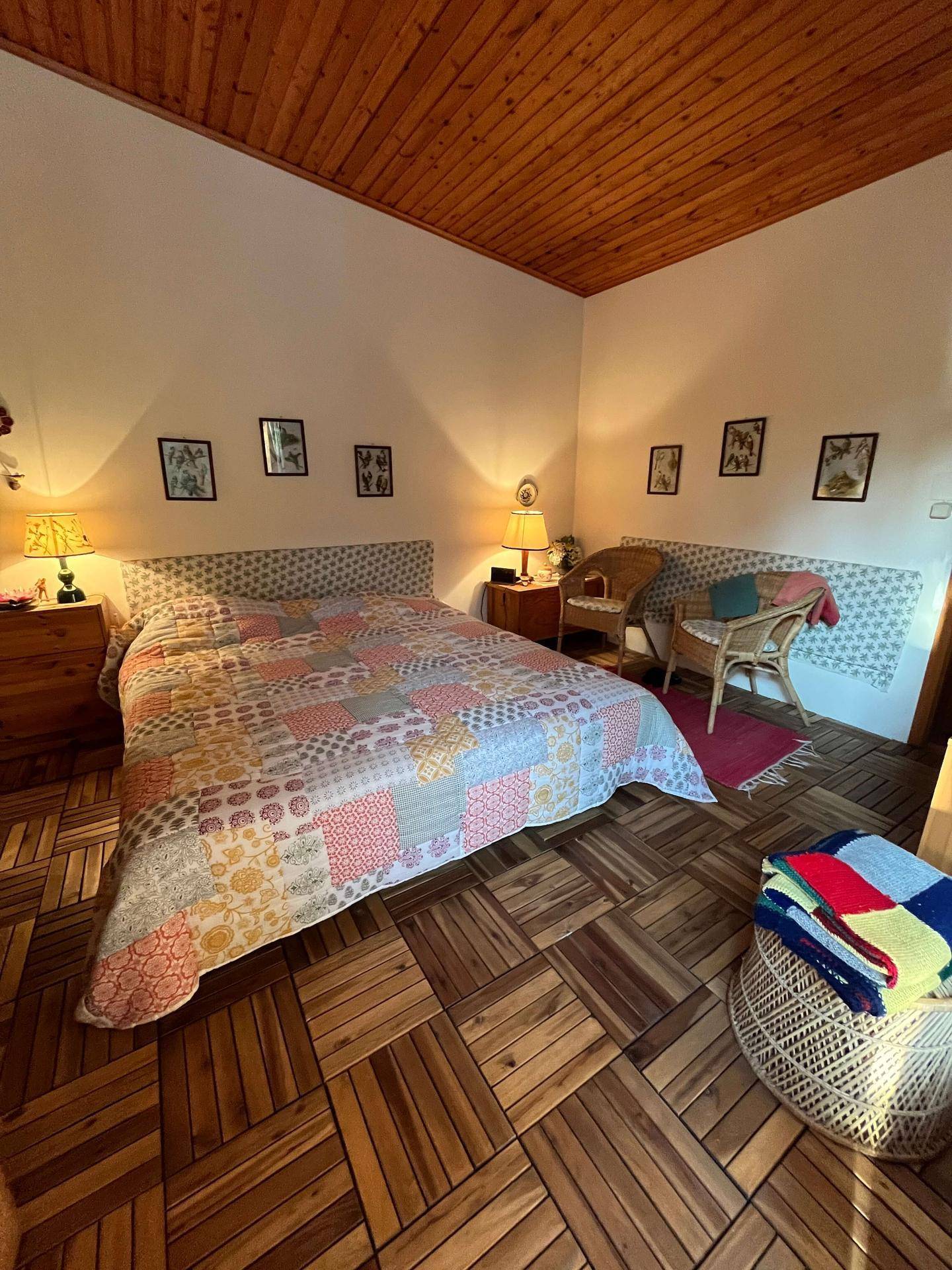 Gemütliches Schlafzimmer mit Holzboden, Holzdecke und einem großen Bett mit bunter Tagesdecke.