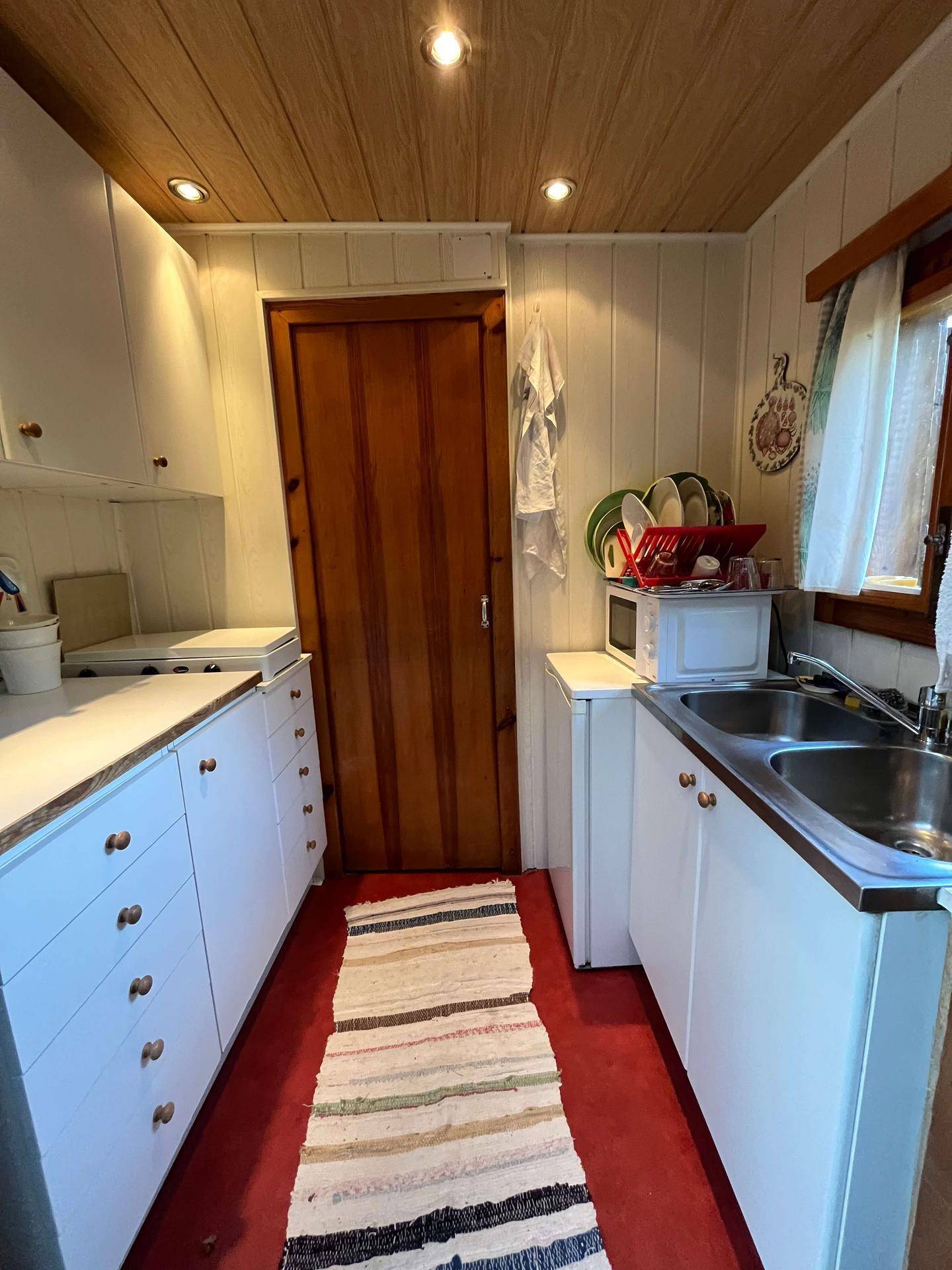 Kleine, funktionale Küche mit weißen Schränken, Holzdecke und rotem Boden.