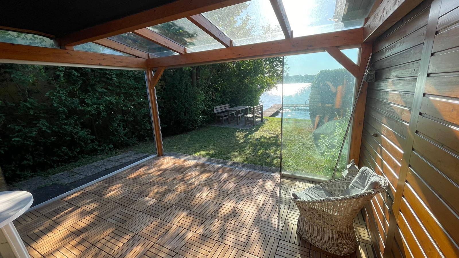 Geräumiger Wintergarten mit Holzboden und Panoramafenstern, die einen weiten Blick ins Grüne bieten.