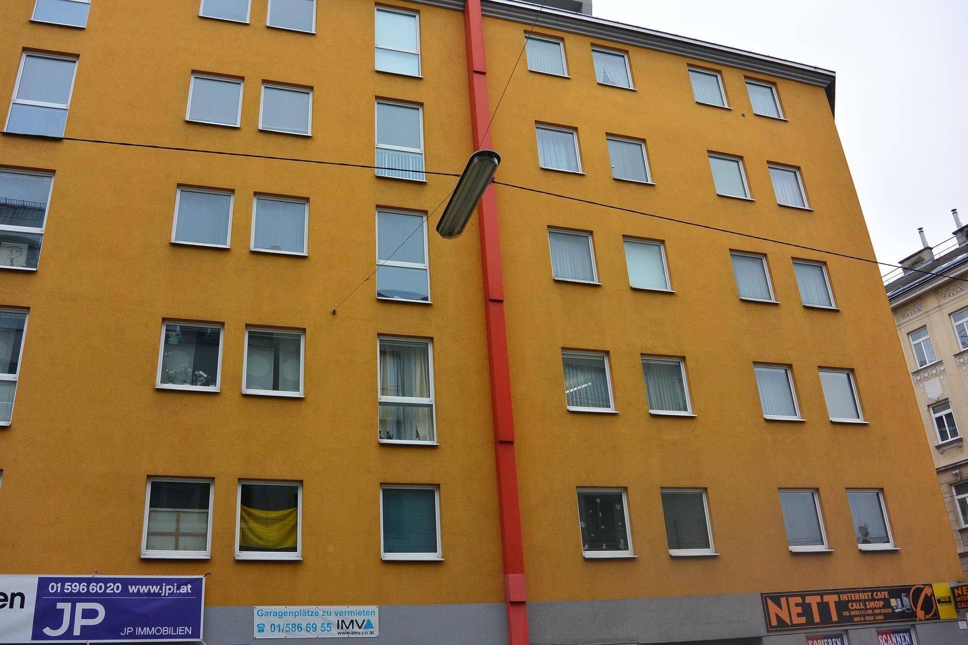 Nahaufnahme der gelben Fassade eines Mehrfamilienhauses mit zahlreichen Fenstern.