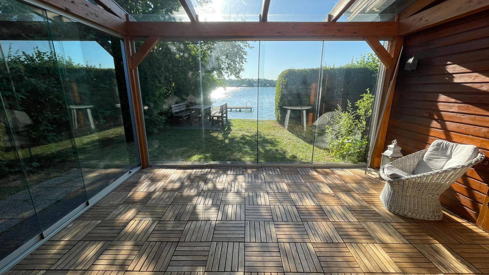 Heller Wintergarten mit Glaswänden, Holzboden und Blick auf den See und den Garten.