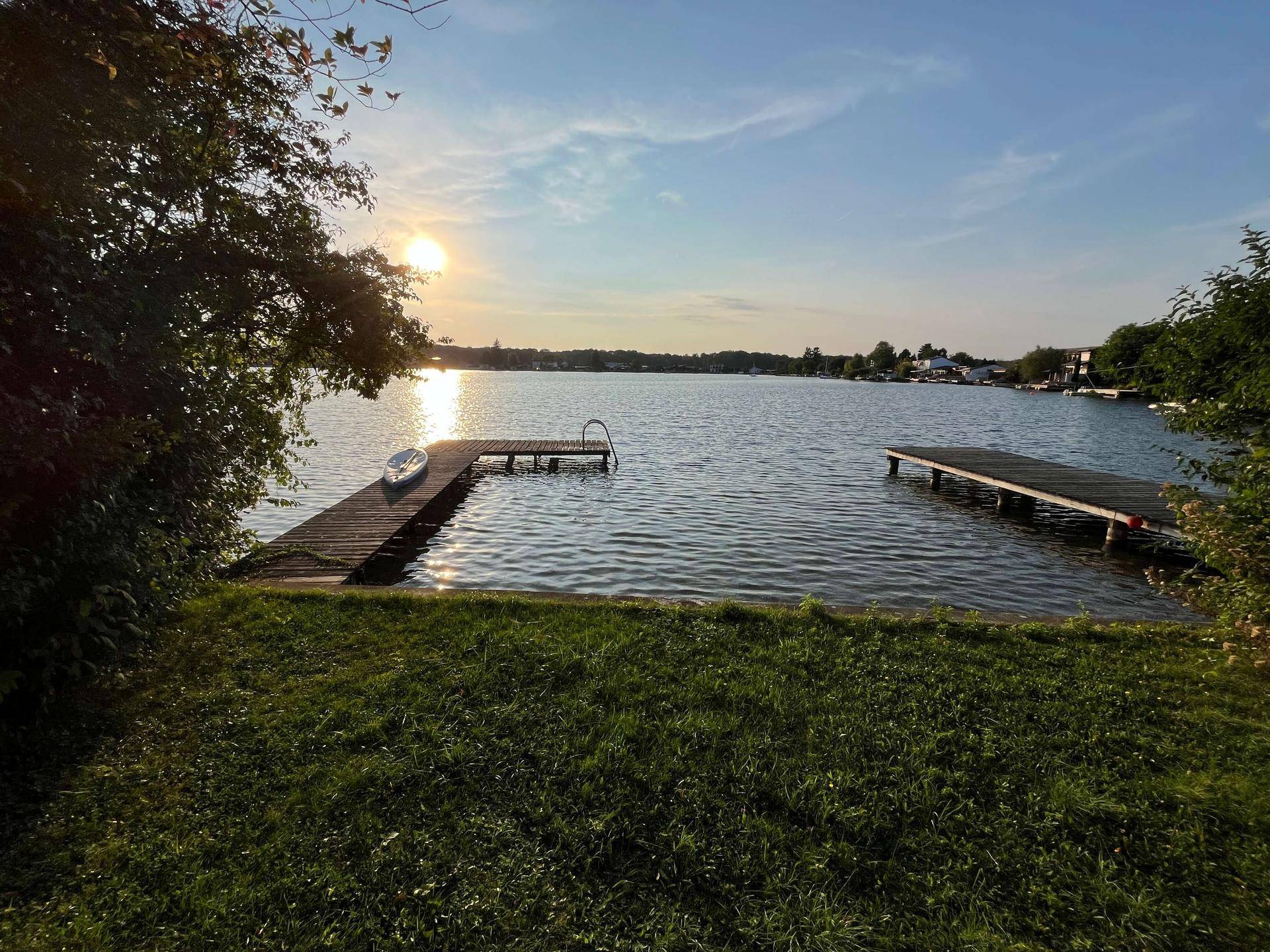 Ruhiger Seeblick bei Sonnenuntergang mit Holzsteg und spiegelndem Wasser.