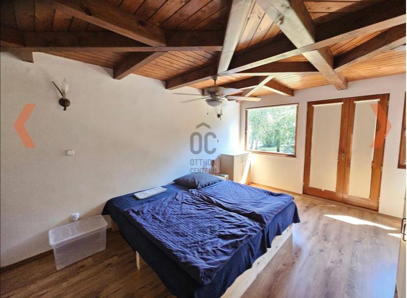Helles Schlafzimmer mit Holzbalkendecke, großem Fenster und Zugang zu weiteren Räumen.