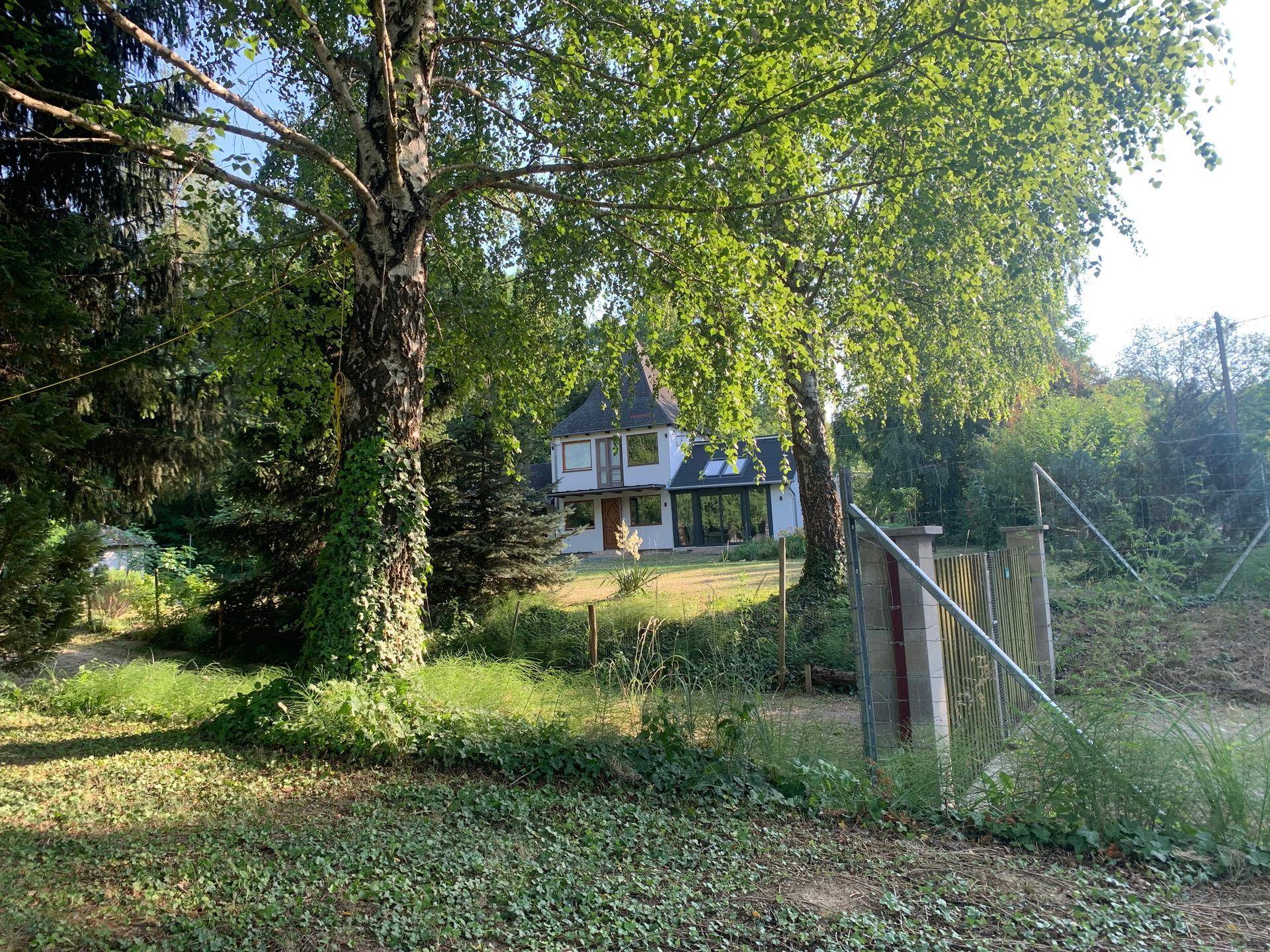 Das Haus eingebettet in eine grüne Landschaft, umgeben von hohen Bäumen und Natur.