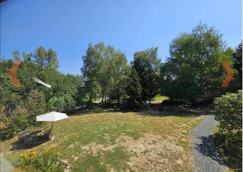 Weitläufiger Gartenbereich mit Rasenfläche und einem möblierten Sitzplatz unter einem Sonnenschirm.