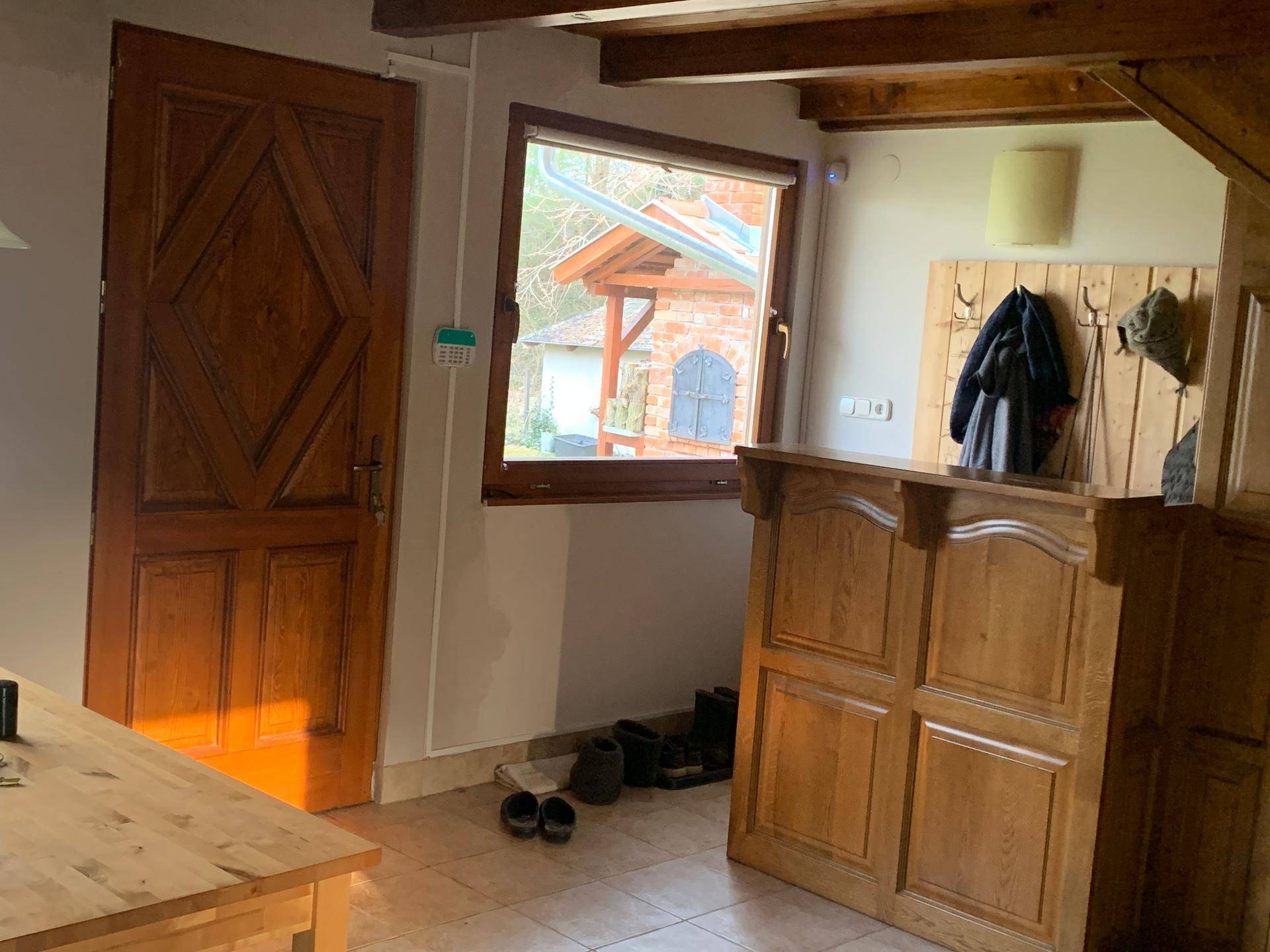 Eingangsbereich mit Holztür, Garderobe und Fliesenboden, hell durch ein Fenster.