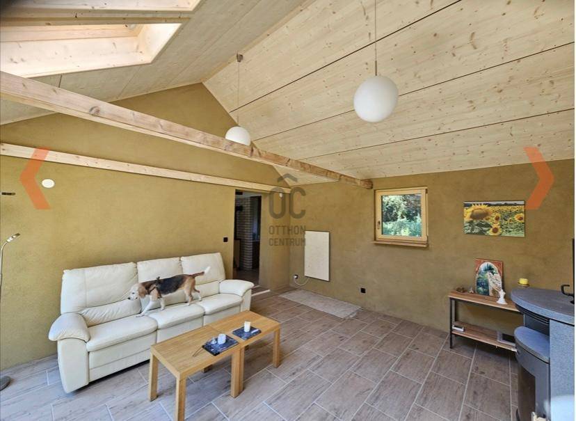 Gemütliches Wohnzimmer mit Holzbalkendecke, beiger Couch und Blick auf den Garten.
