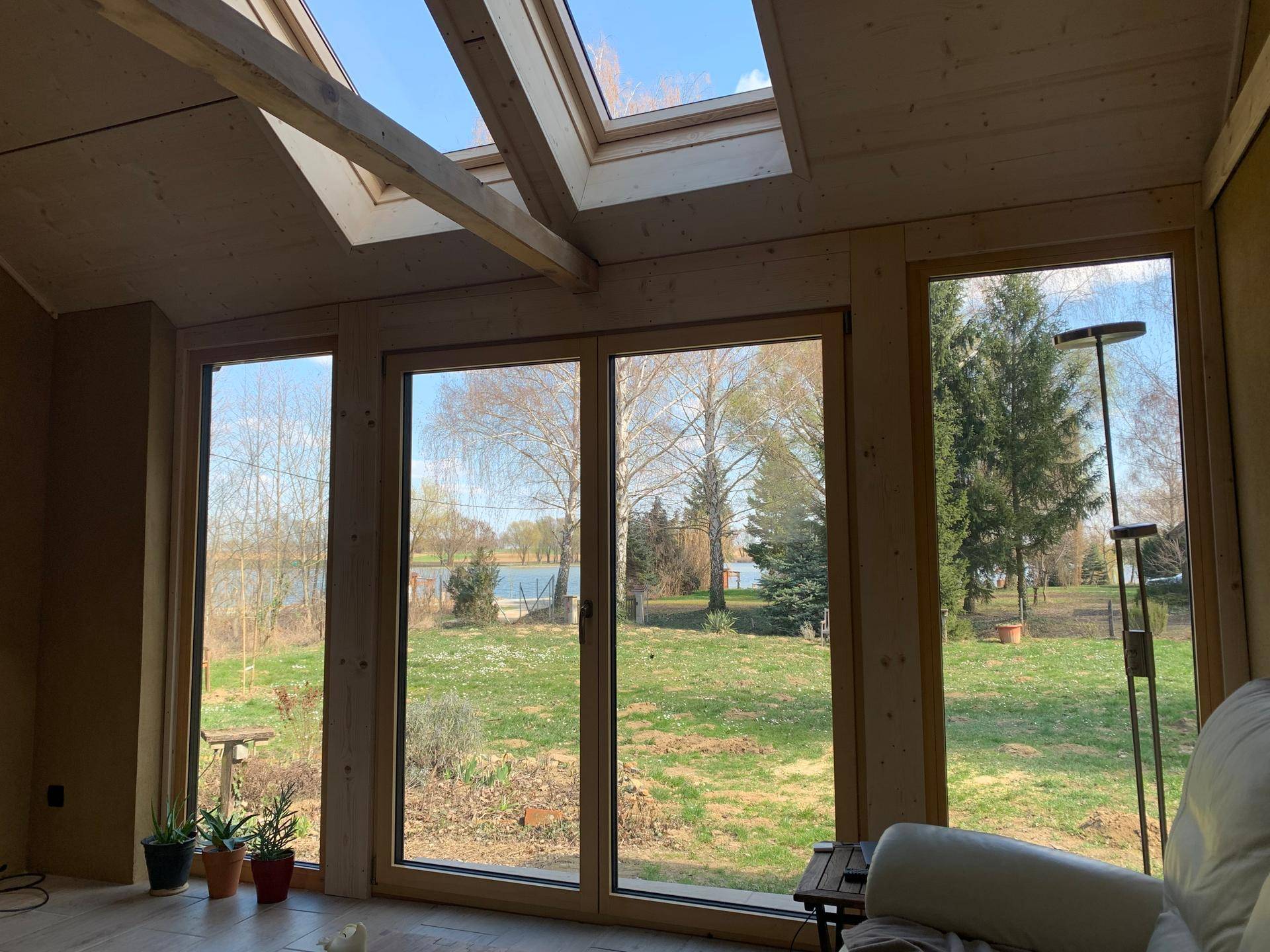 Weitläufiger Blick auf den See und den Garten durch große Fenster in einem hellen Raum.