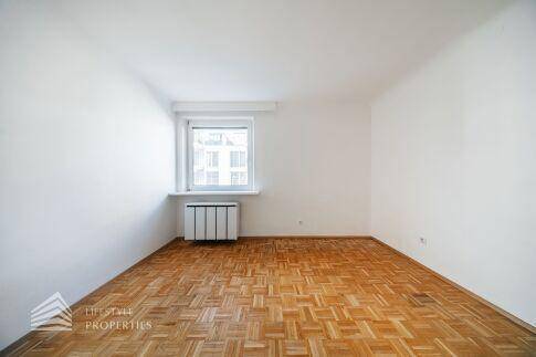 Lichtdurchflutetes Zimmer mit klassischem Parkettboden und einem großen Fenster.