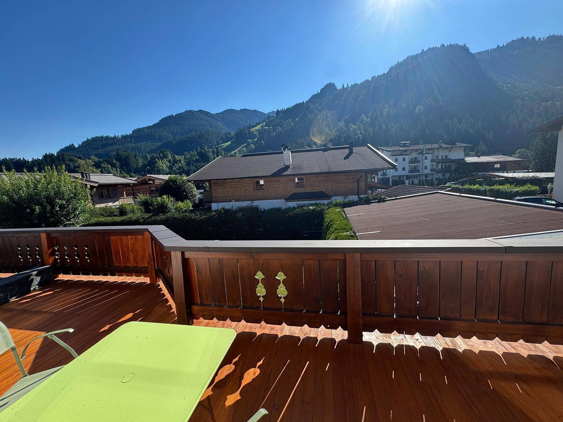 Sonniger Balkon mit Holzboden, Sitzgelegenheiten und einem weiten Blick auf die Berge.