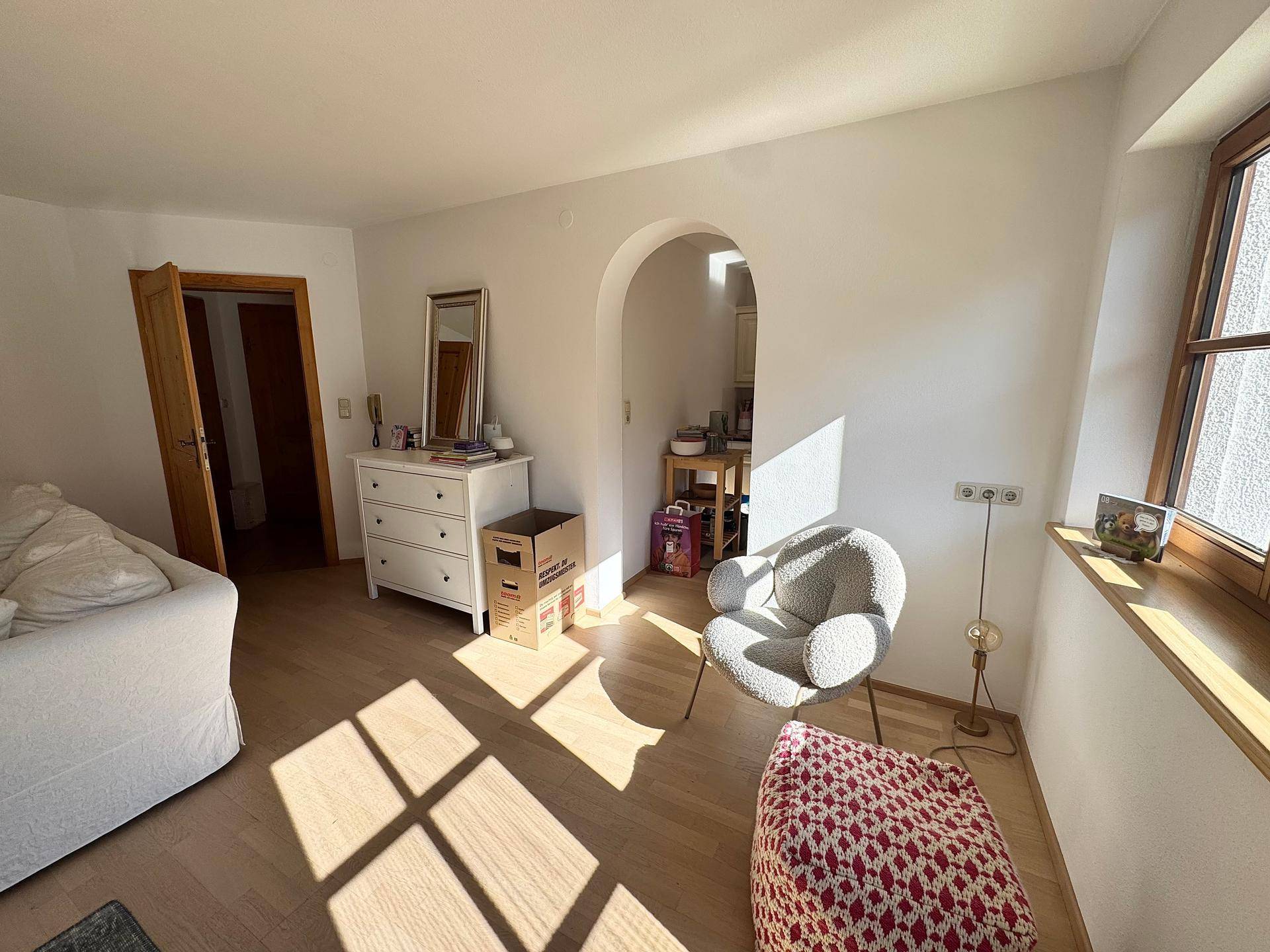 Heller Wohnbereich mit einem dekorativen Bogen und einem Fenster, das viel Sonnenlicht hereinlässt.