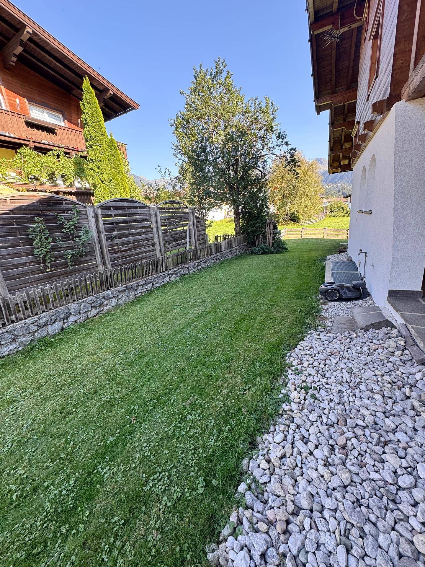 Gepflegter Gartenbereich mit Rasenfläche, Kiesweg und einem Holzzaun.