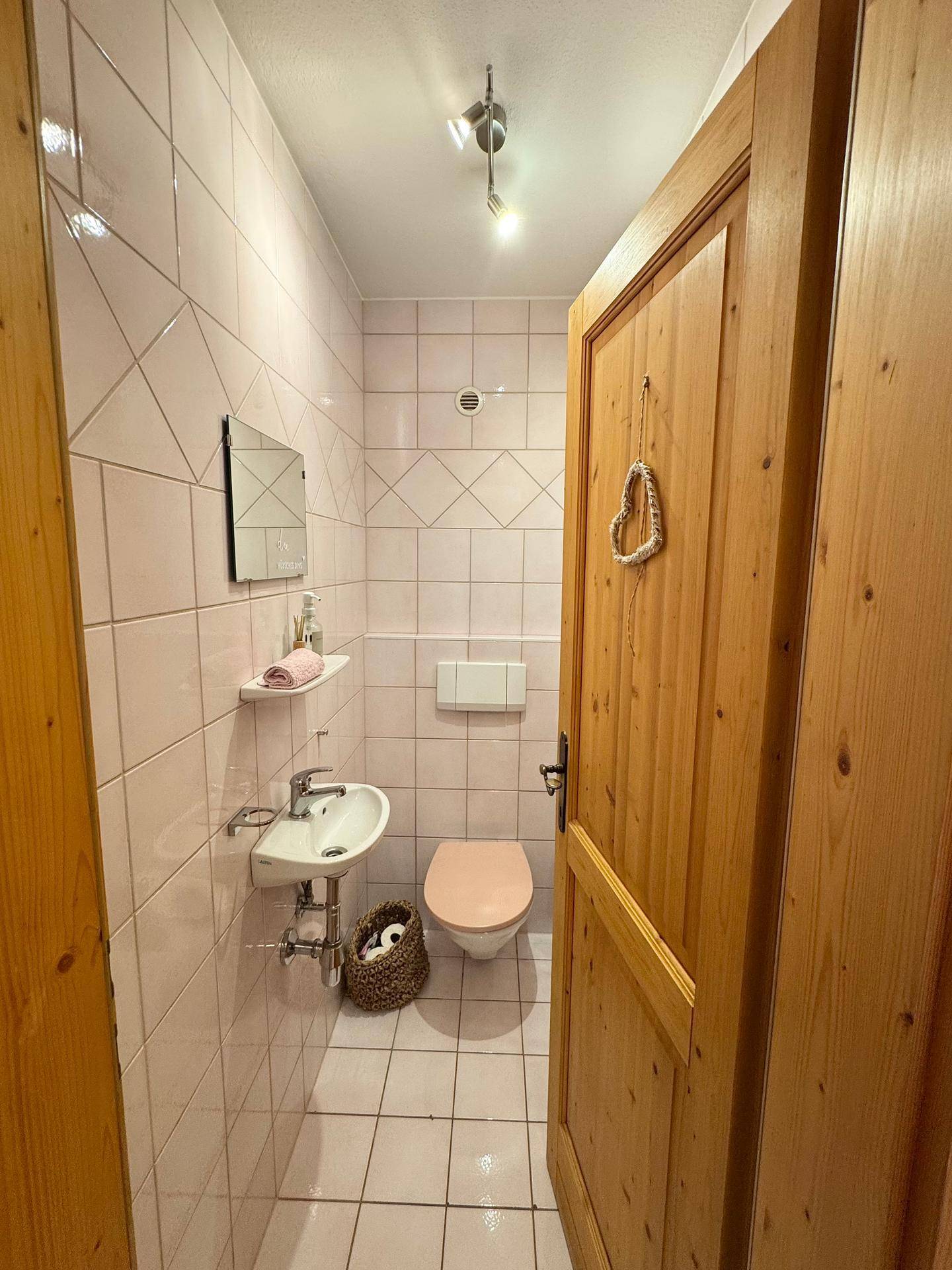 Separates Gäste-WC mit rosa Fliesen, Toilette und einem kleinen Handwaschbecken.