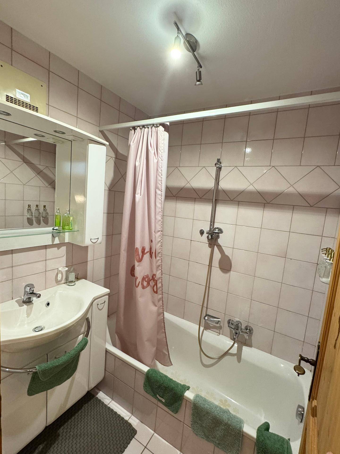 Badezimmer mit rosa Fliesen, einer Badewanne mit Duschfunktion und einem Waschbecken.