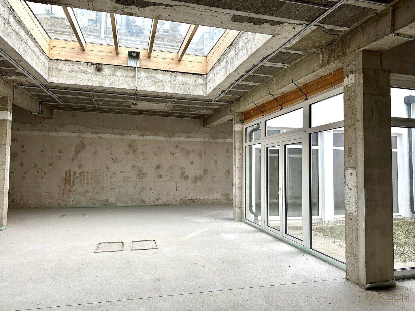 Eine weitere Ansicht des unfertigen Innenraums, die das große Oberlicht und die Fensterfront hervorhebt.
