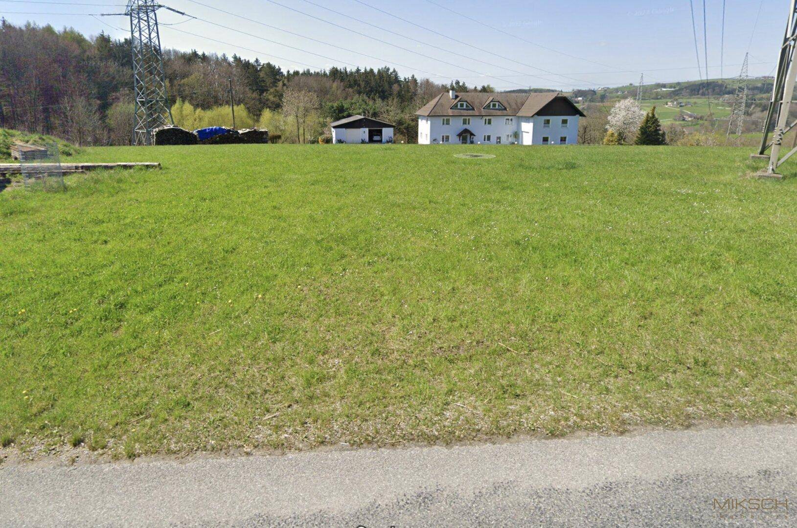 Ländliche Umgebung mit einem weißen Wohnhaus, Nebengebäude und weiten Grünflächen.
