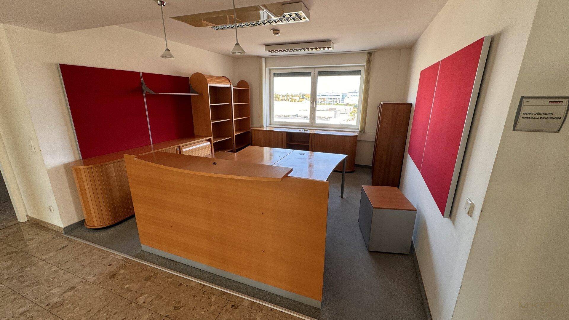 Geräumiges Büro mit Teppichboden, modernen Möbeln und roten Akzentwänden.