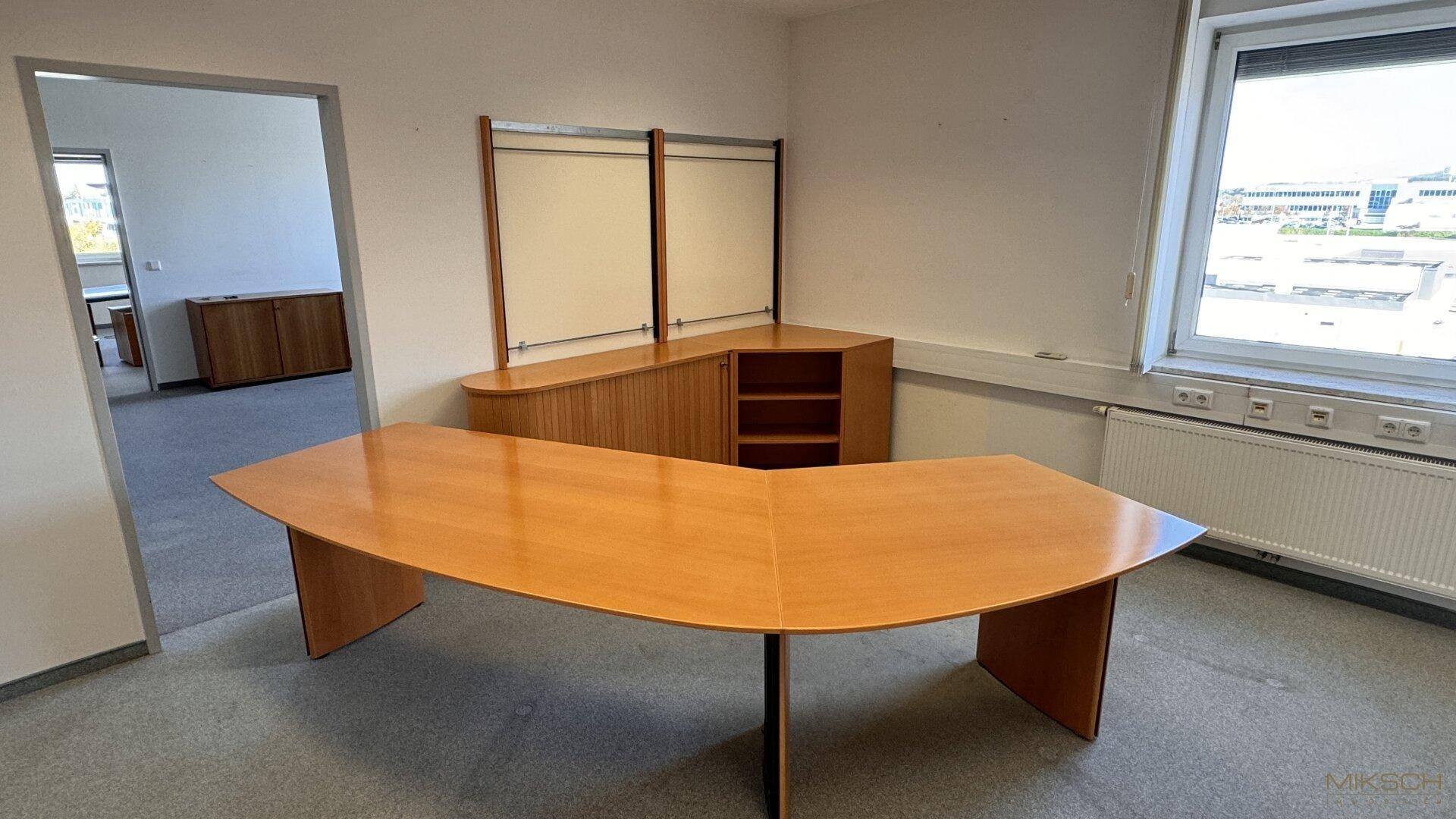 Büro mit Teppichboden, Holzmöbeln und einem großen Schreibtisch in der Mitte des Raumes.