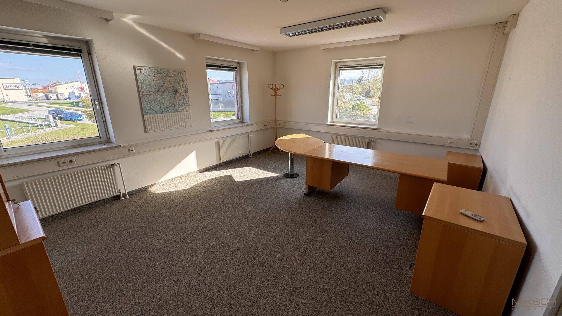 Geräumiges Büro mit mehreren Fenstern, Teppichboden und einem großen Schreibtisch.