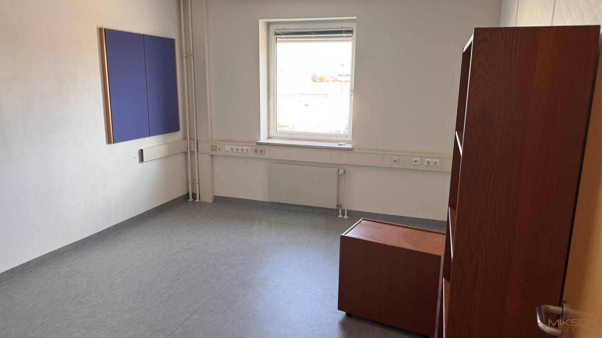 Helles Büro mit grauem Vinylboden, Fenster und einem blauen Akzent an der Wand.