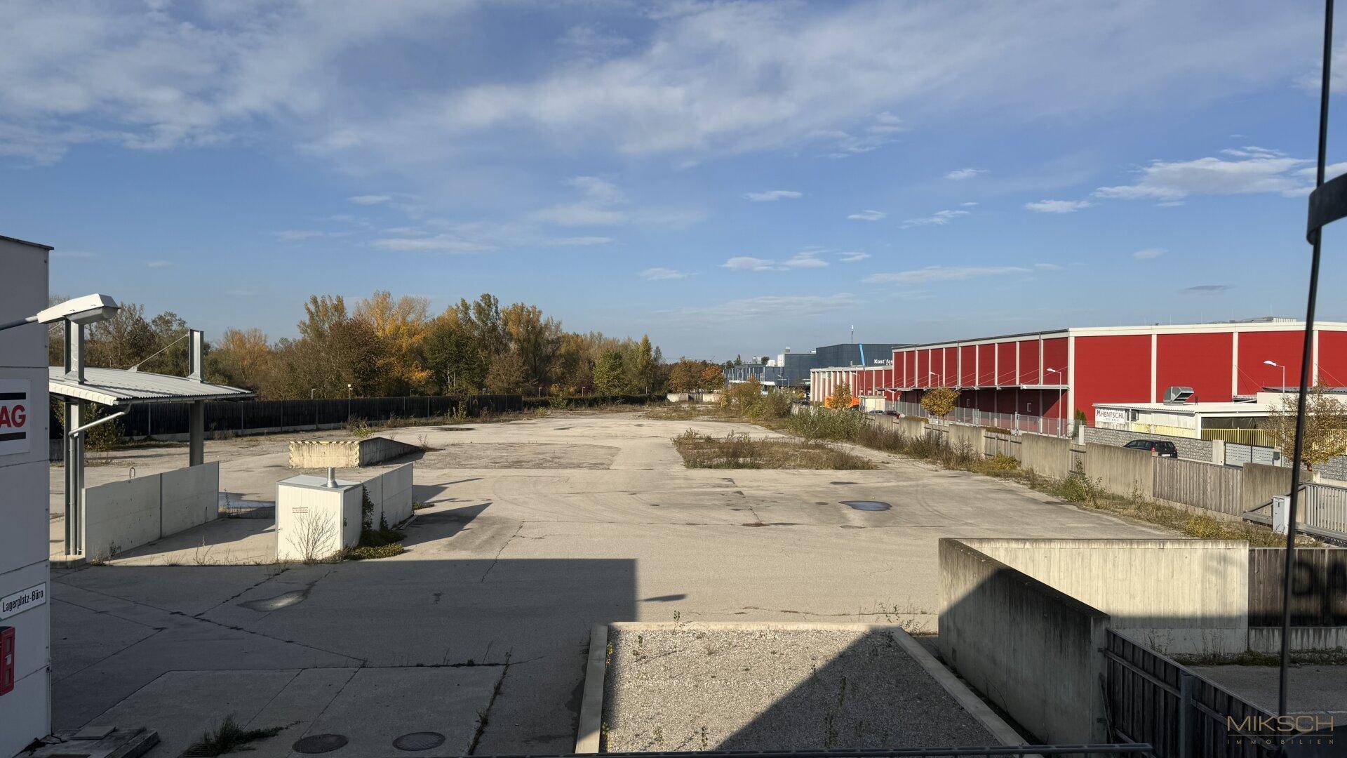 Weitläufiges, leeres Grundstück mit Blick auf umliegende Industriegebäude und Bäume.