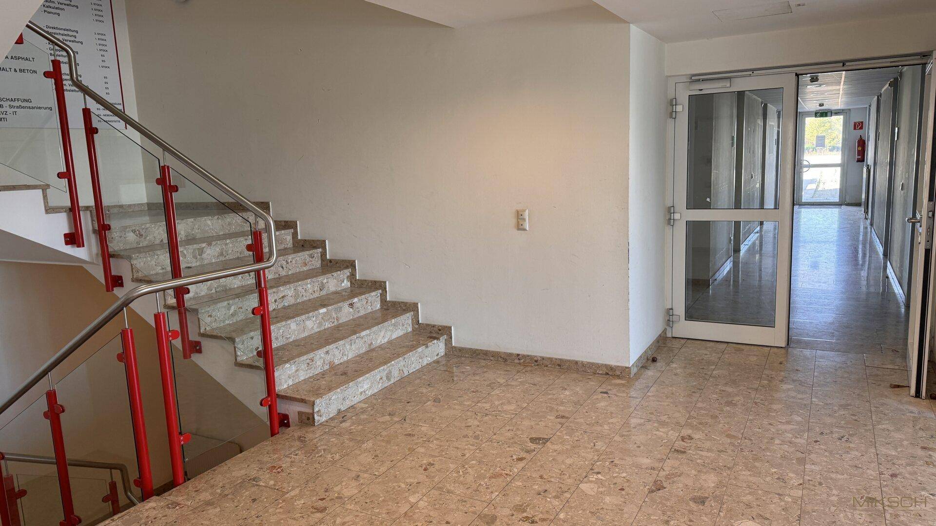 Heller Eingangsbereich mit Steintreppe und einem langen Flur, der zu weiteren Räumen führt.
