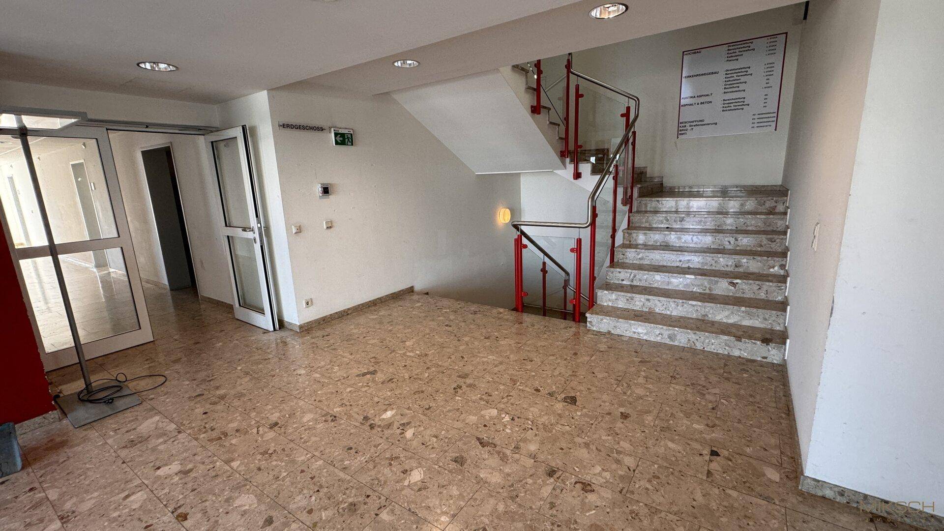 Geräumiger Eingangsbereich mit Marmorboden und einer Treppe mit rotem Geländer.