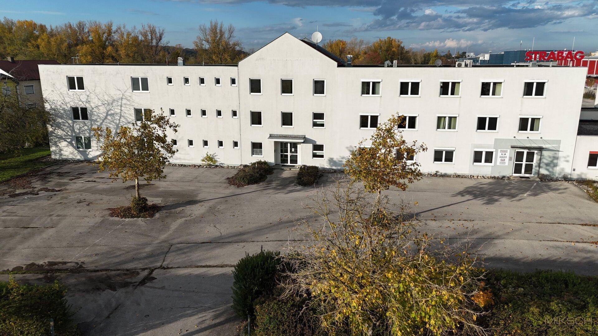 Frontansicht des weißen Geschäftsgebäudes mit vielen Fenstern und einem großen leeren Parkplatz.