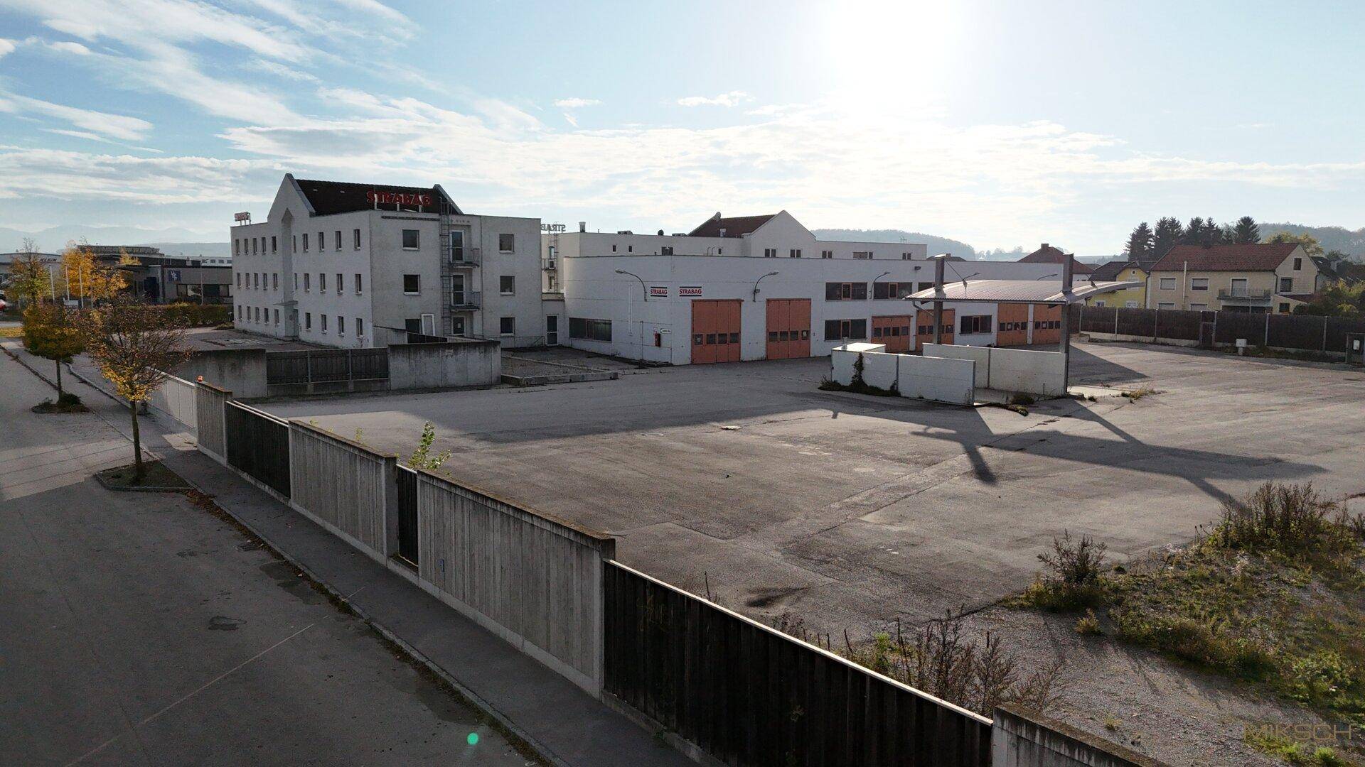 Gesamtansicht des Geschäftsgeländes mit Parkflächen und einer langen Begrenzungsmauer.