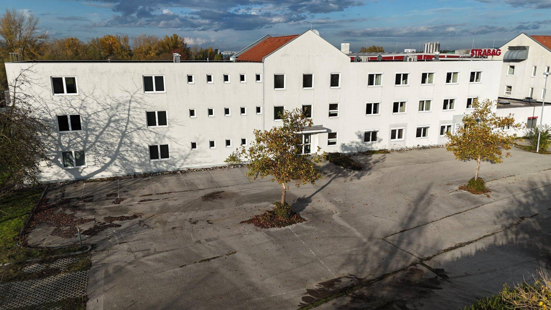 Frontansicht des weißen Geschäftsgebäudes mit Herbstbäumen und einem großen leeren Parkplatz.