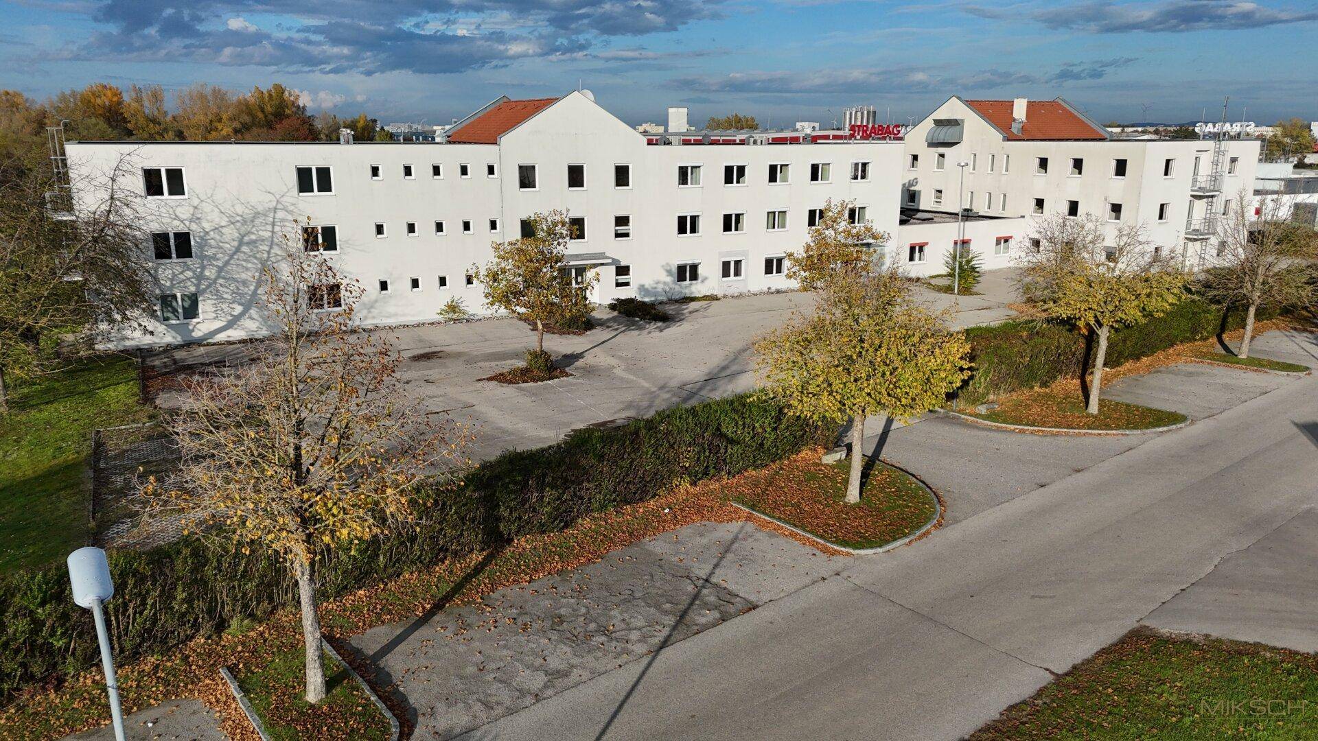 Gesamtansicht des Geschäftsgebäudes mit umliegenden Parkplätzen und herbstlicher Bepflanzung.
