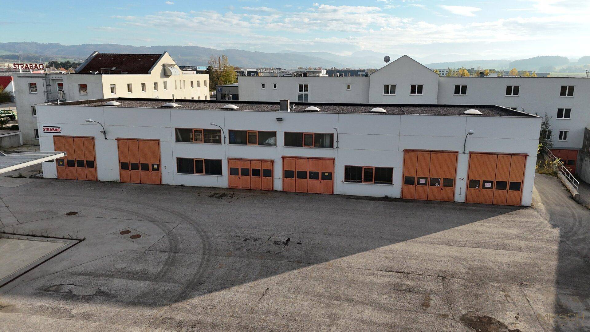 Gebäude mit mehreren orangefarbenen Garagentoren und einem großen, leeren Vorplatz.