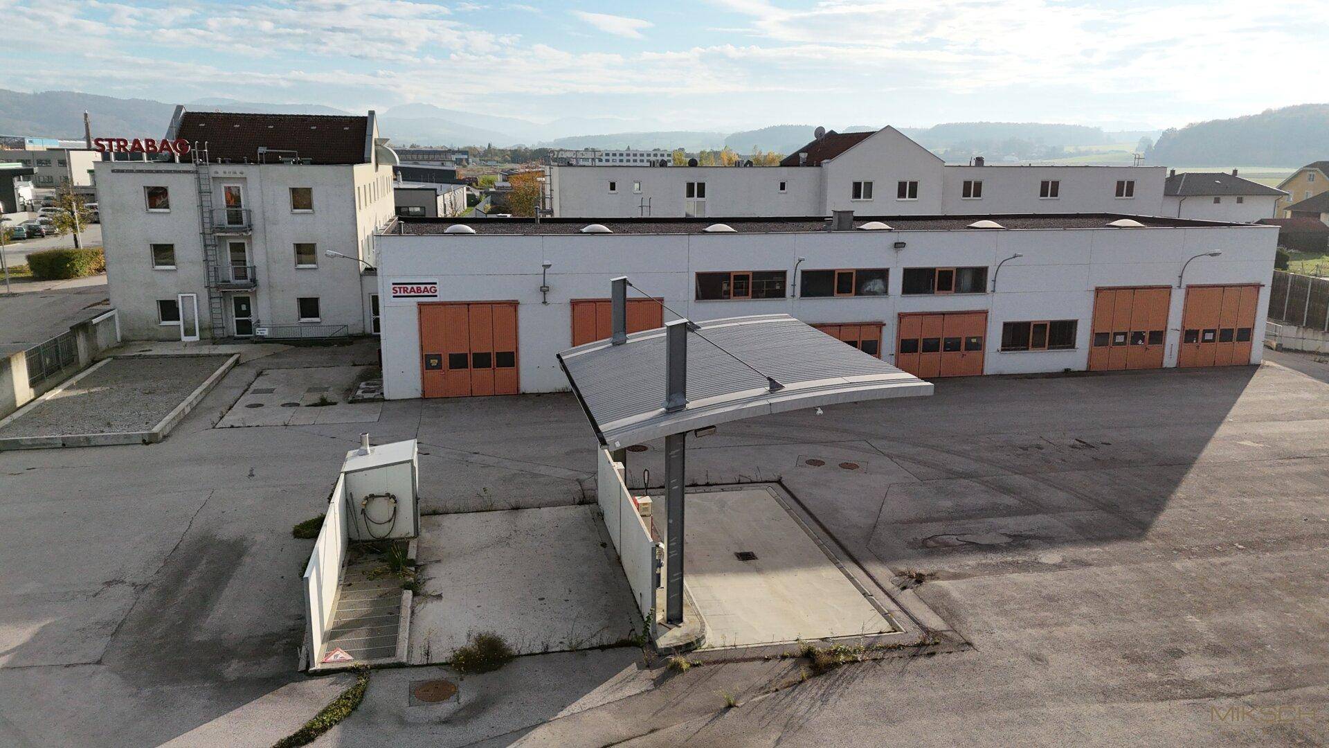 Geschäftskomplex mit einer überdachten Struktur auf dem Parkplatz und angrenzenden Hallen.