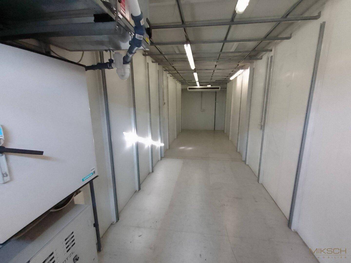 Heller Technikraum mit Schaltschränken, Lüftungsanlagen und Leuchtstoffröhren an der Decke.