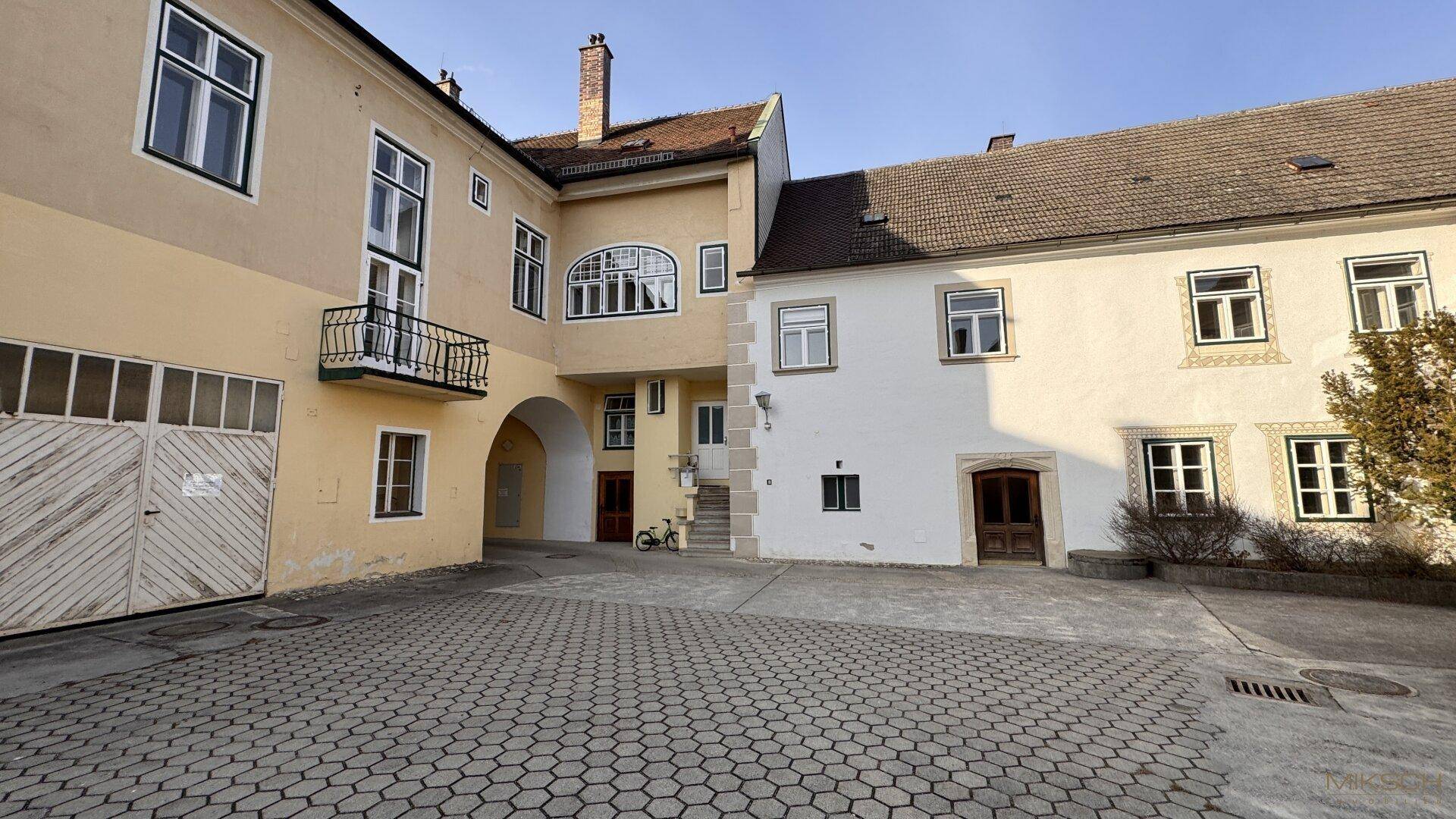Innenhof mit Kopfsteinpflaster, verschiedenen Gebäudeteilen und einem kleinen Balkon.