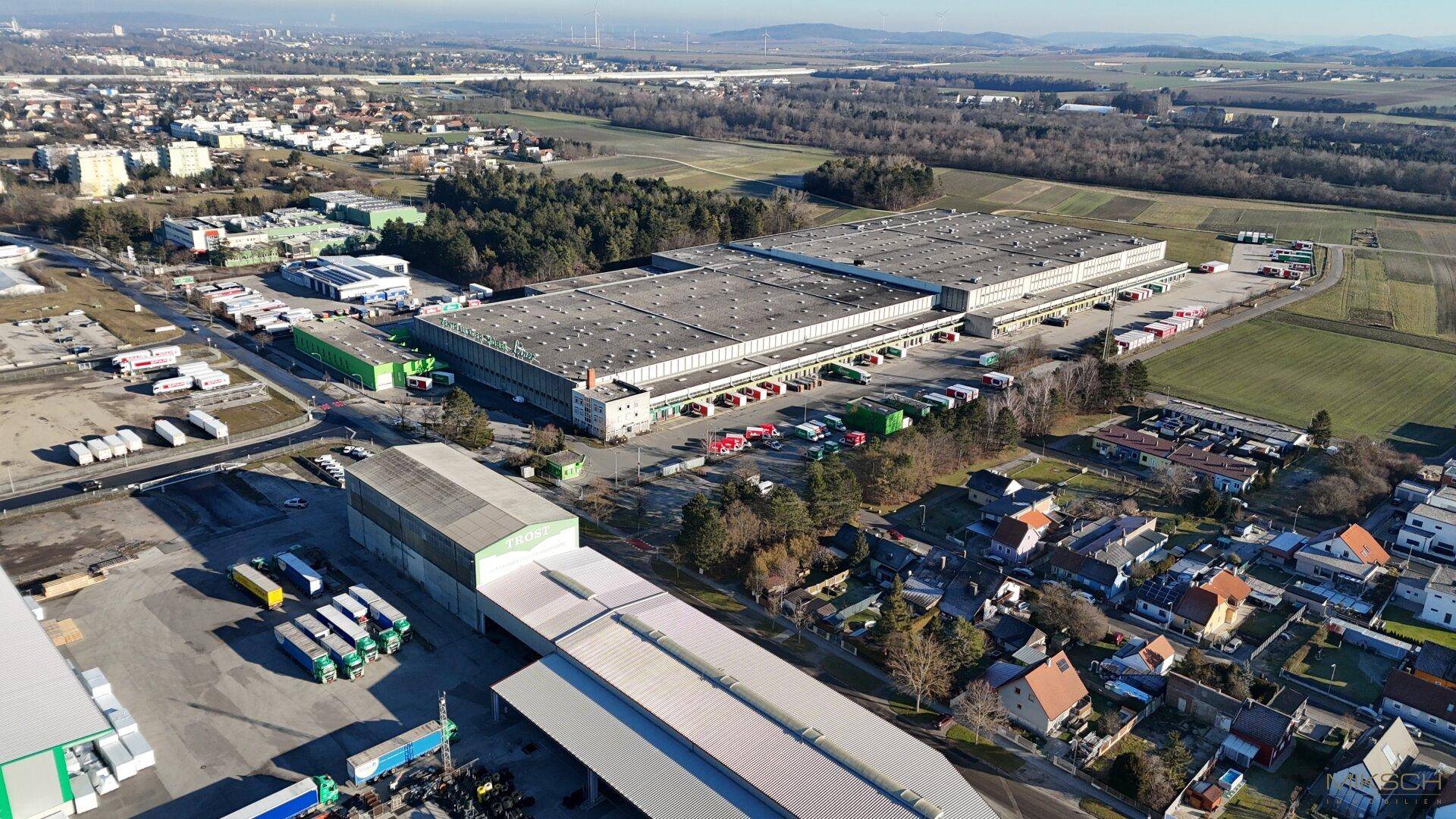 Überblick aus der Luft über das weitläufige Logistikareal mit umliegender Infrastruktur und Naturlandschaft.