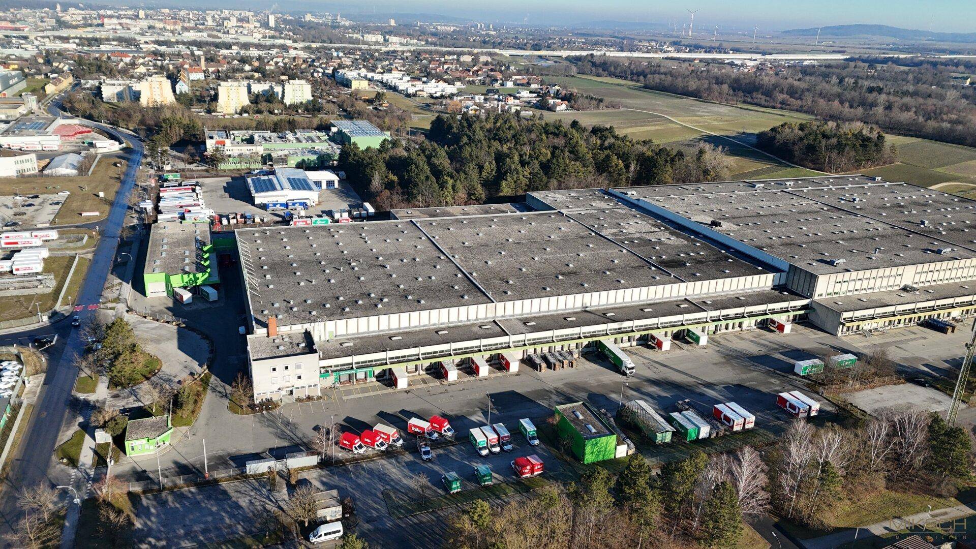 Weitläufige Luftaufnahme eines Logistikzentrums mit angrenzenden Feldern und Wohngebieten im Hintergrund.