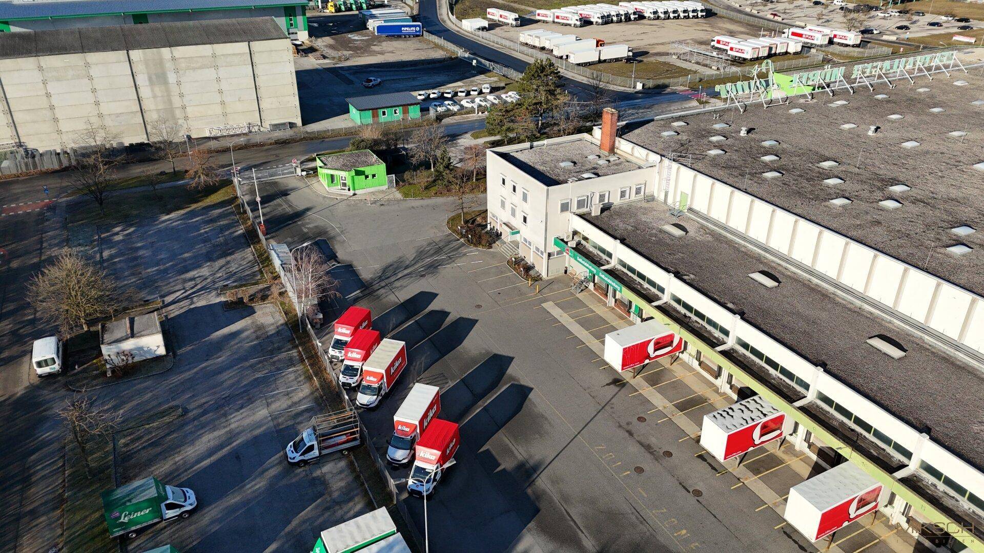 Detailaufnahme des Hauptgebäudes mit Bürotrakt, Laderampen und angrenzenden Parkplätzen für Mitarbeiter und Lieferanten.