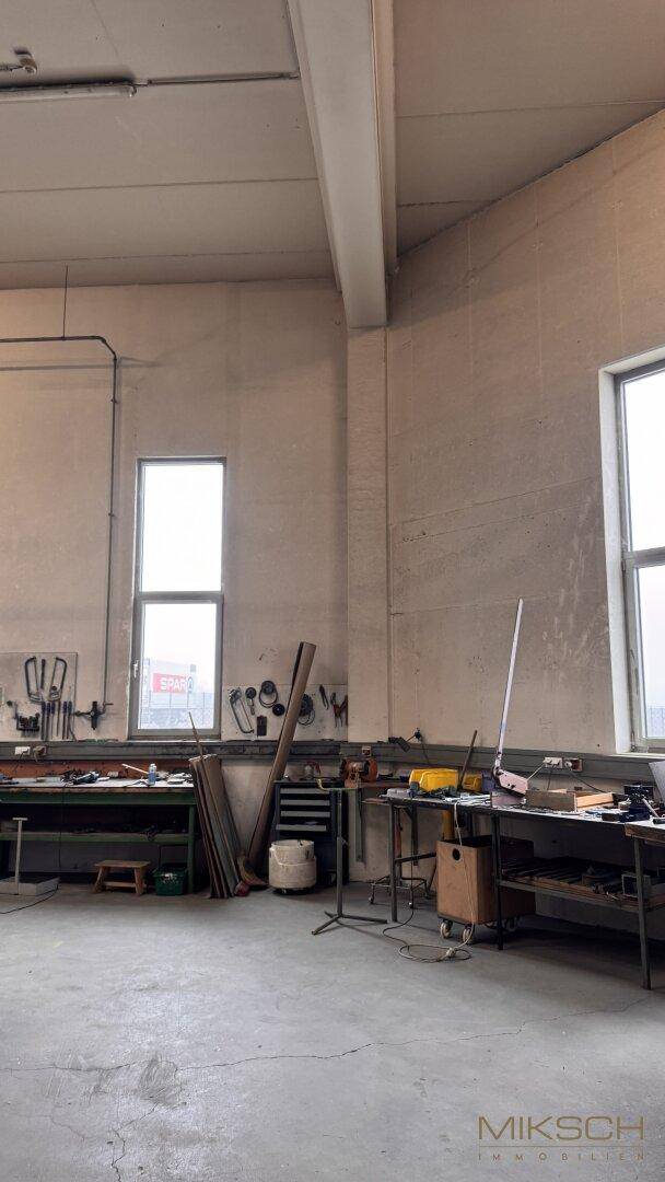 Werkstattbereich mit Arbeitsflächen, Werkzeugen an der Wand und hohen Fenstern für Tageslicht.