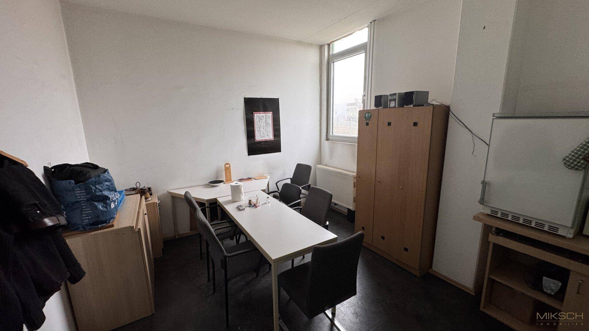 Aufenthaltsraum mit Tischen, Stühlen und einem Schrank, ideal für Pausen oder Besprechungen.