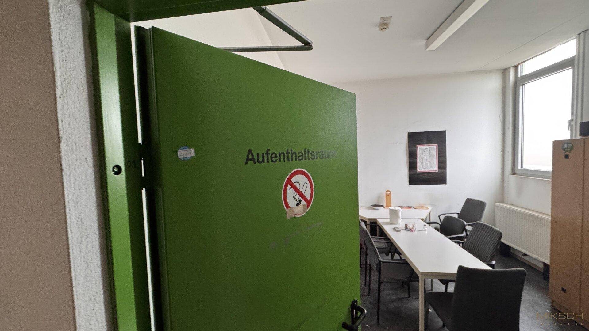 Eingang zum Aufenthaltsraum mit grüner Tür und Hinweisschildern, die auf die Nutzung hinweisen.