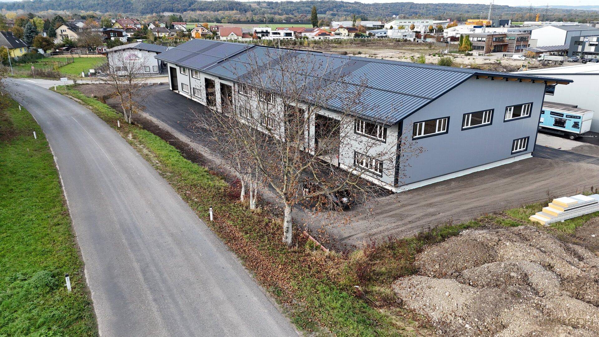 Weitläufige Luftaufnahme einer modernen Gewerbehalle in ländlicher Umgebung mit angrenzender Straße.