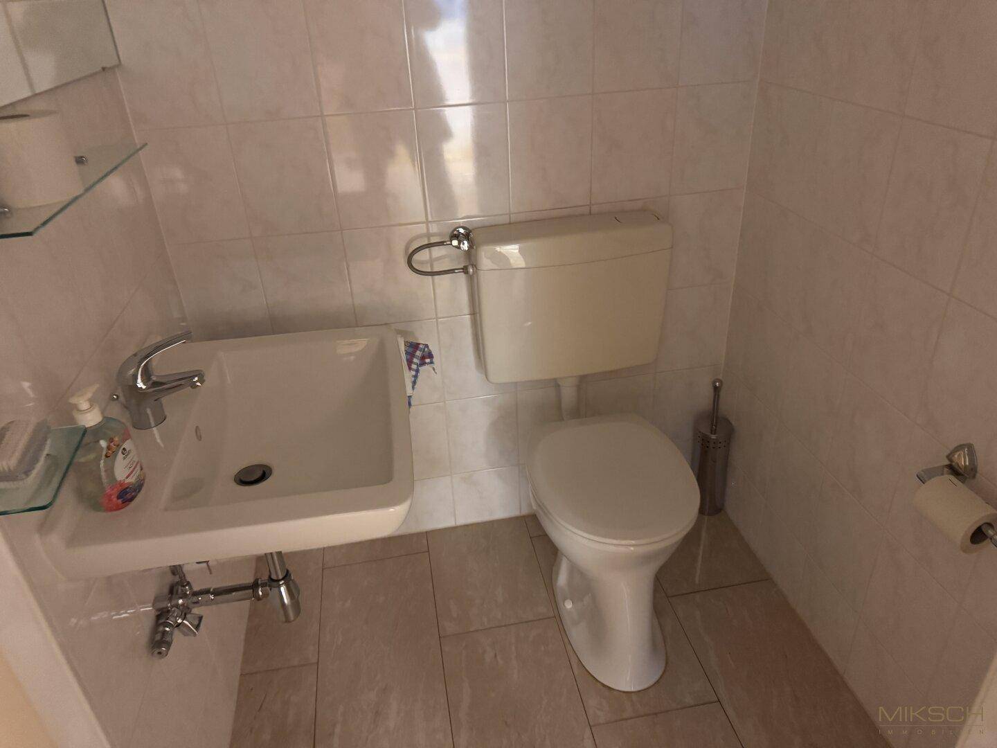 Kompakte Gästetoilette mit weißen Wandfliesen, kleinem Waschbecken und funktionaler Ausstattung.