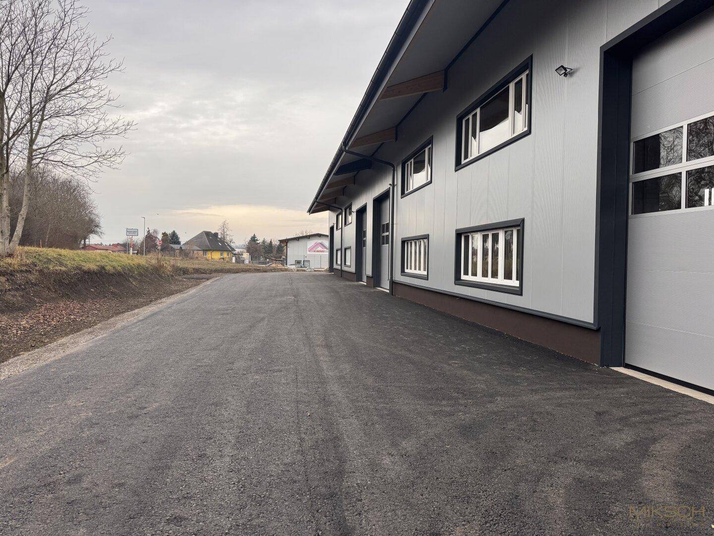 Seitenansicht der Gewerbehalle mit Sektionaltoren und Fenstern, umgeben von einem Zufahrtsweg.