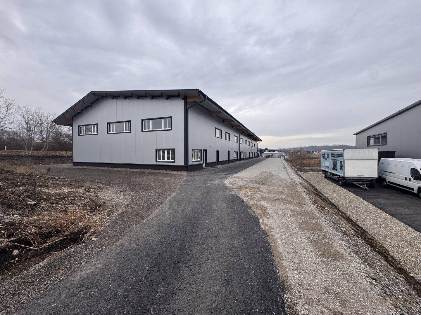 Seitenansicht der Gewerbehalle mit Zufahrtsweg und Blick auf die ländliche Umgebung.